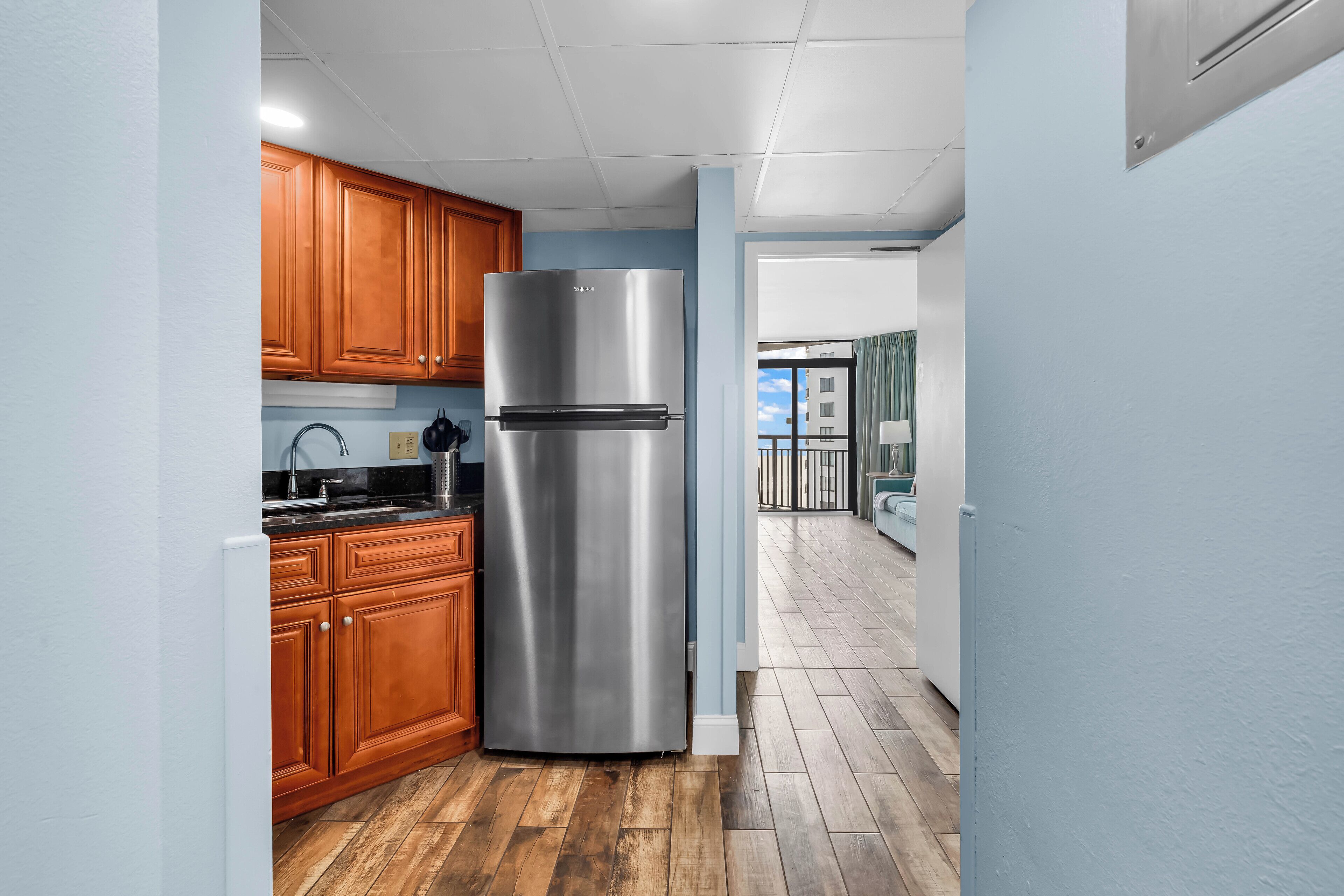 A modern kitchen with wooden cabinets, a stainless steel refrigerator, and a wooden floor.