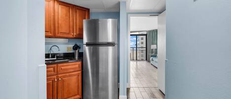 A modern kitchen with wooden cabinets, a stainless steel refrigerator, and a wooden floor.