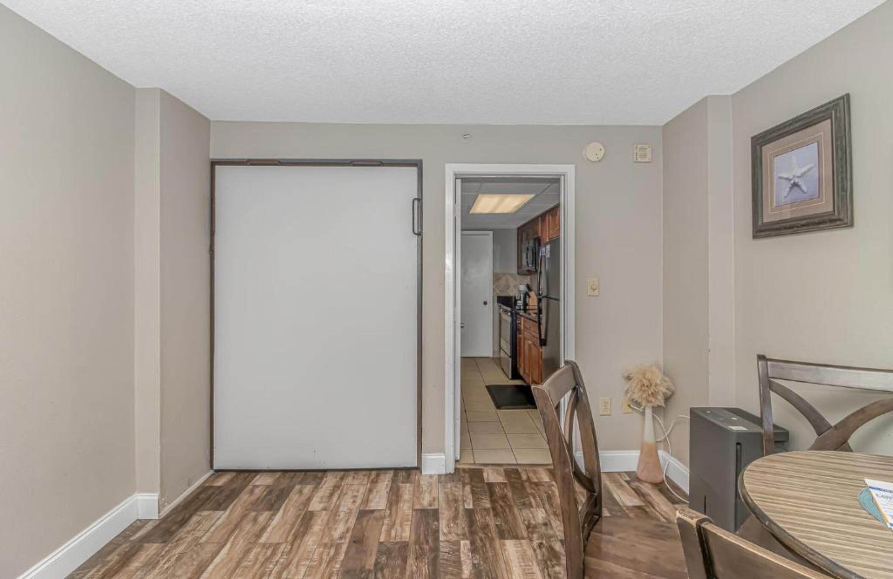 A hallway with a closed door, a dining area with a table and chairs, and a kitchen visible through an open door.