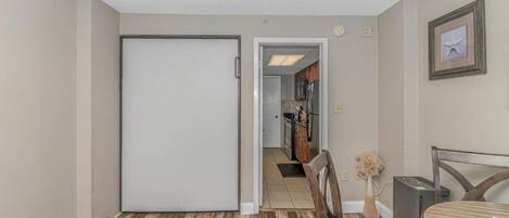 A hallway with a closed door, a dining area with a table and chairs, and a kitchen visible through an open door.