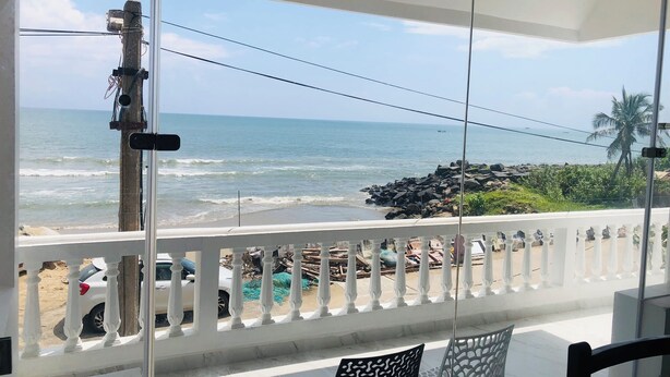 A balcony with a view of the ocean, white railing, and a table with chairs. - Virtus home stay  (Puducherry)