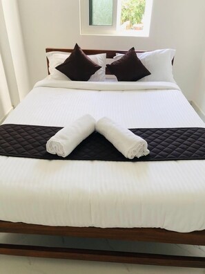 A neatly made bed with white linens, two dark pillows, and a quilted headboard.