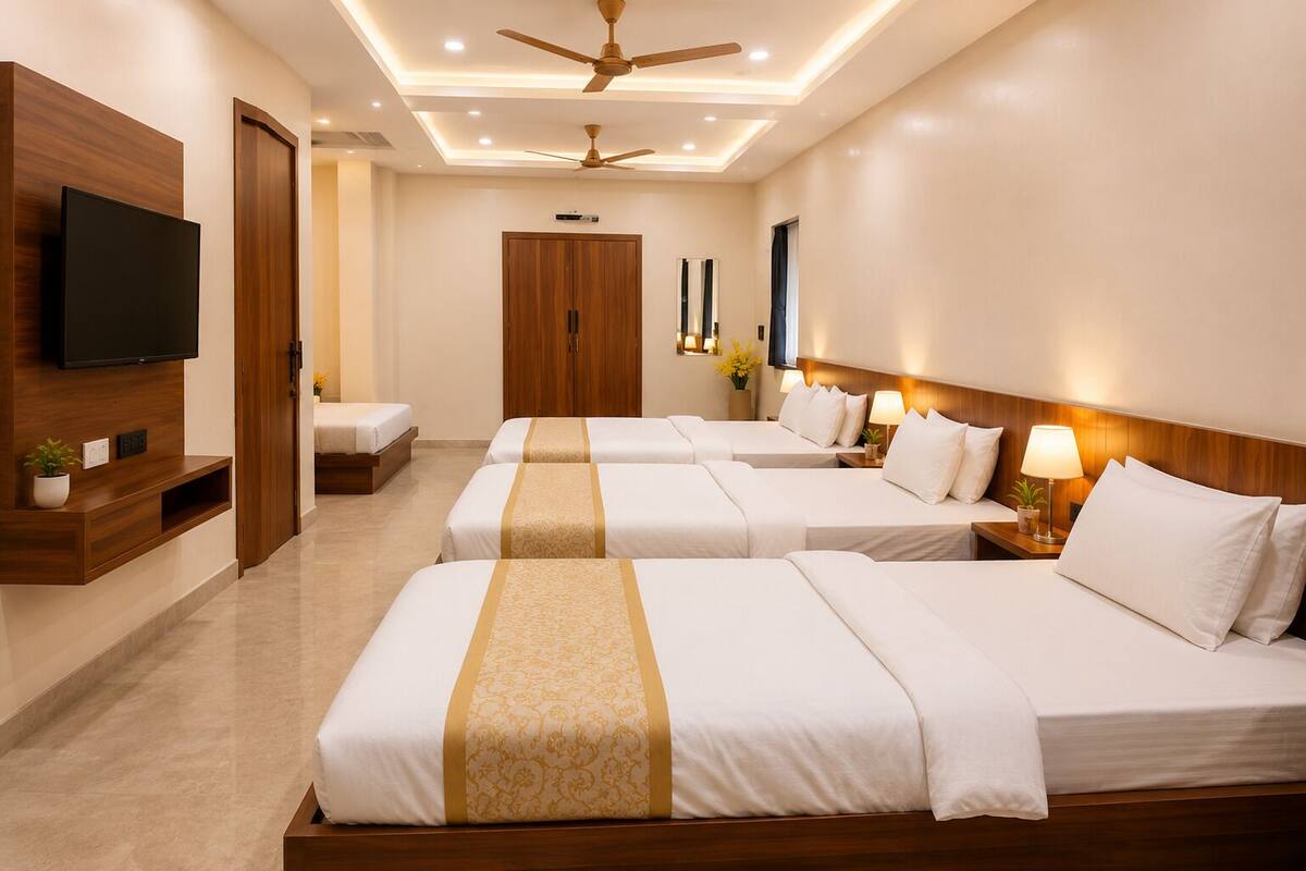 A hotel room with three beds, a TV, wooden furniture, and a ceiling fan.
