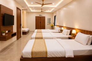 A hotel room with three beds, a TV, wooden furniture, and a ceiling fan. - Hotel Maa Annpurna Palace (Ujjain)