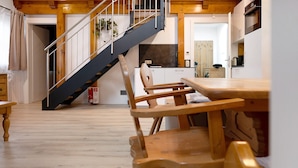 Una escalera de madera que conduce a un segundo piso, un comedor con sillas y mesa de madera, y una cocina con armarios y electrodomésticos.
