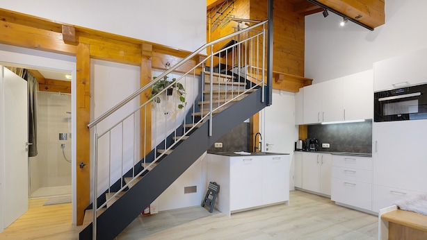 Una cocina moderna con armarios blancos, encimera negra y escalera de acero inoxidable.