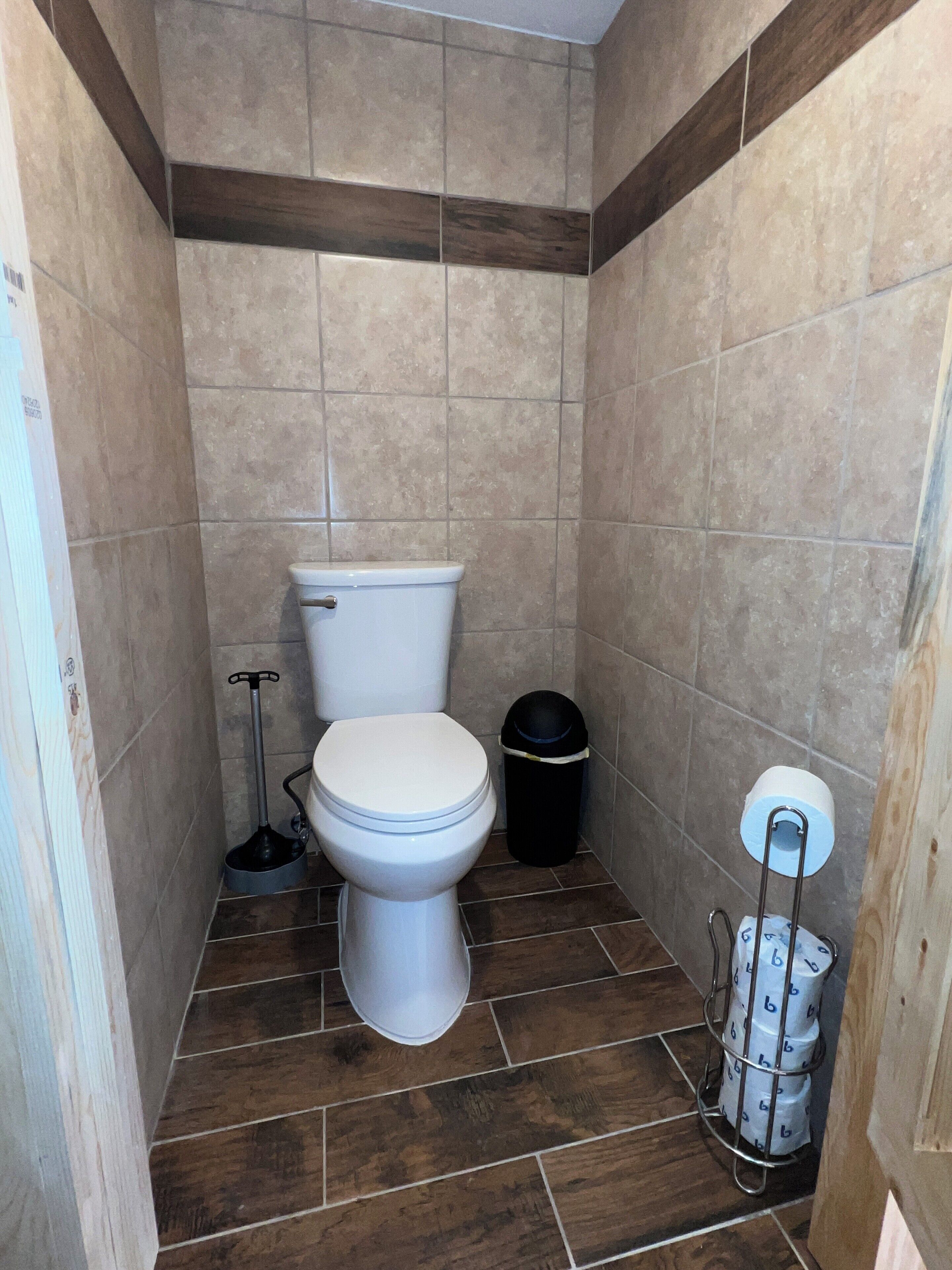 Ein kleines Badezimmer mit Toilette, einem schwarzen Mülleimer und einem Metallregal für Toilettenpapier.