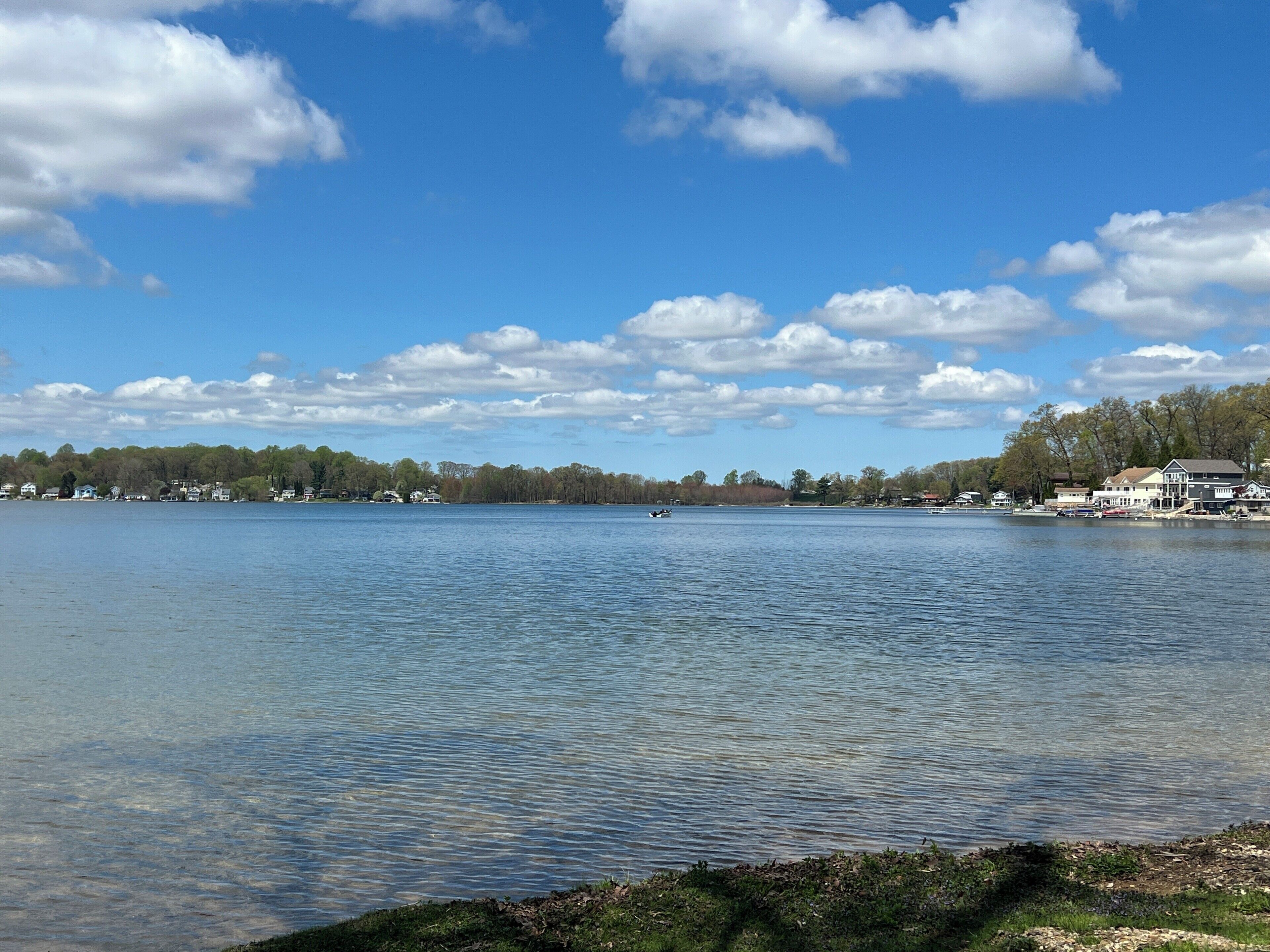 A lake with a boat, houses along the shore, and trees in the background.