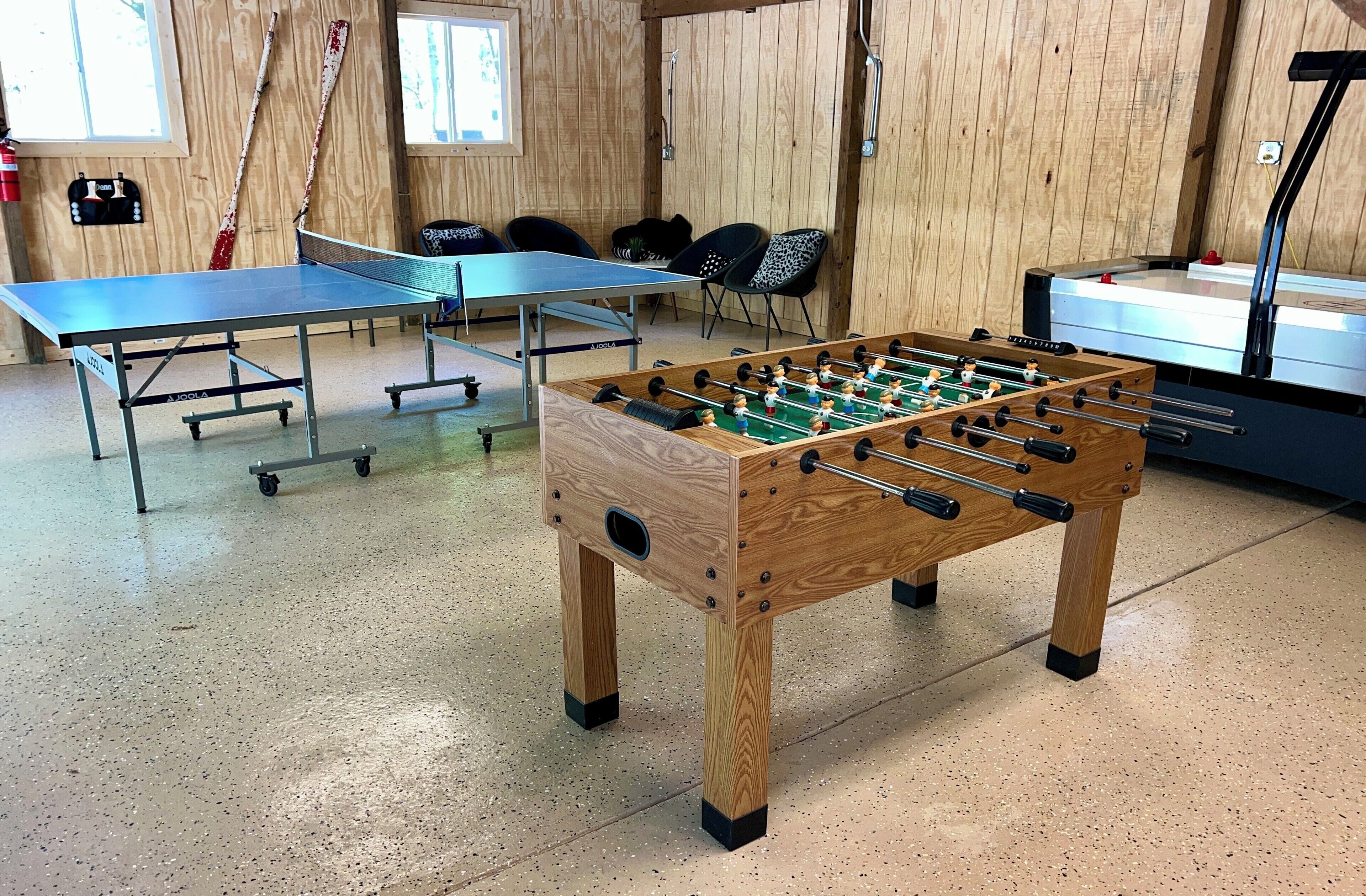 Ett rum med ett bordtennisbord, ett fotbollsspel och ett fotbollsspel med träinlägg.