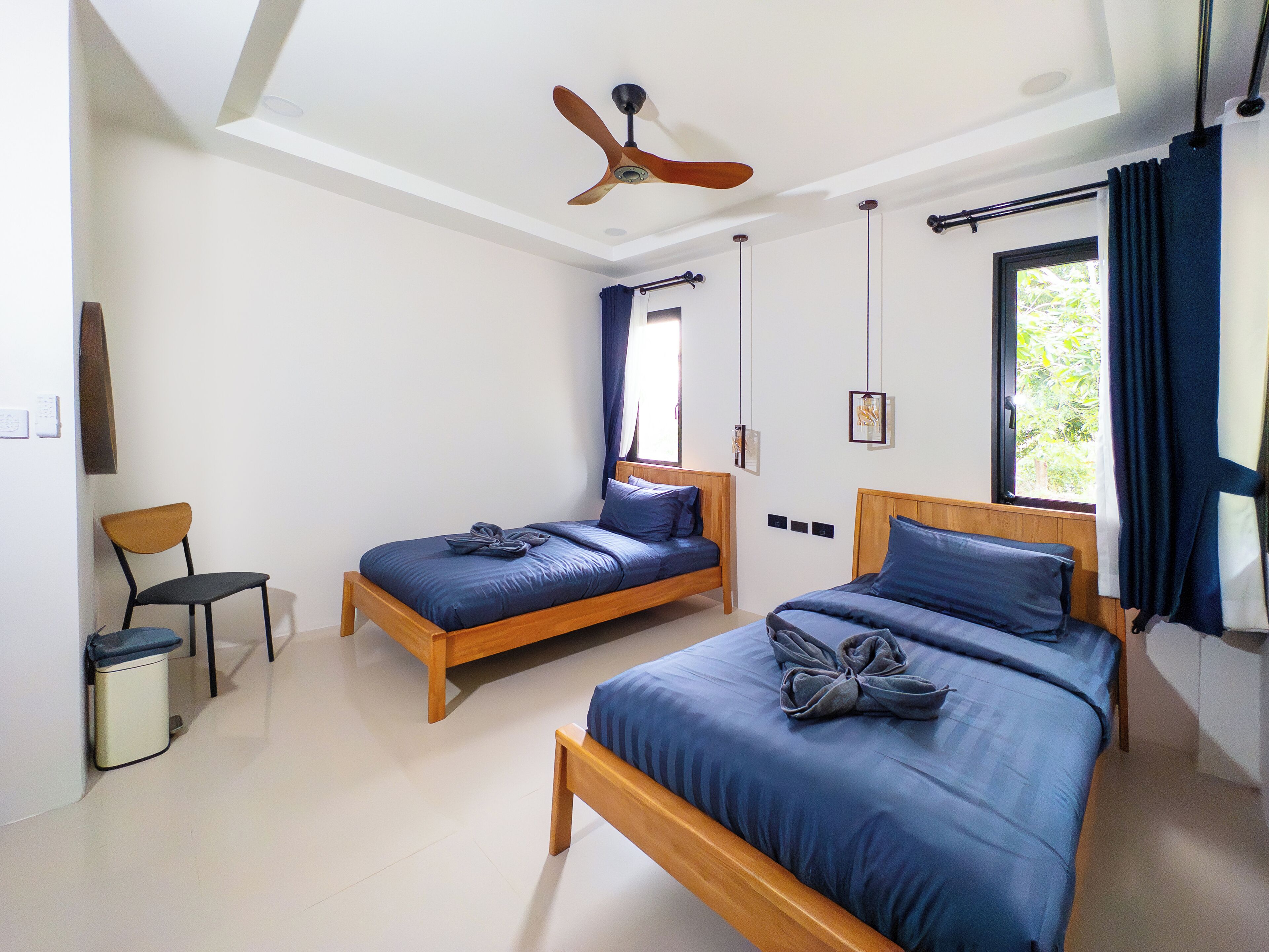 Une chambre à coucher avec deux lits en bois, un ventilateur de plafond et une fenêtre avec des rideaux.