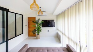Un interior moderno con un sofá, una planta en maceta, una puerta de madera y un televisor montado en la pared.
