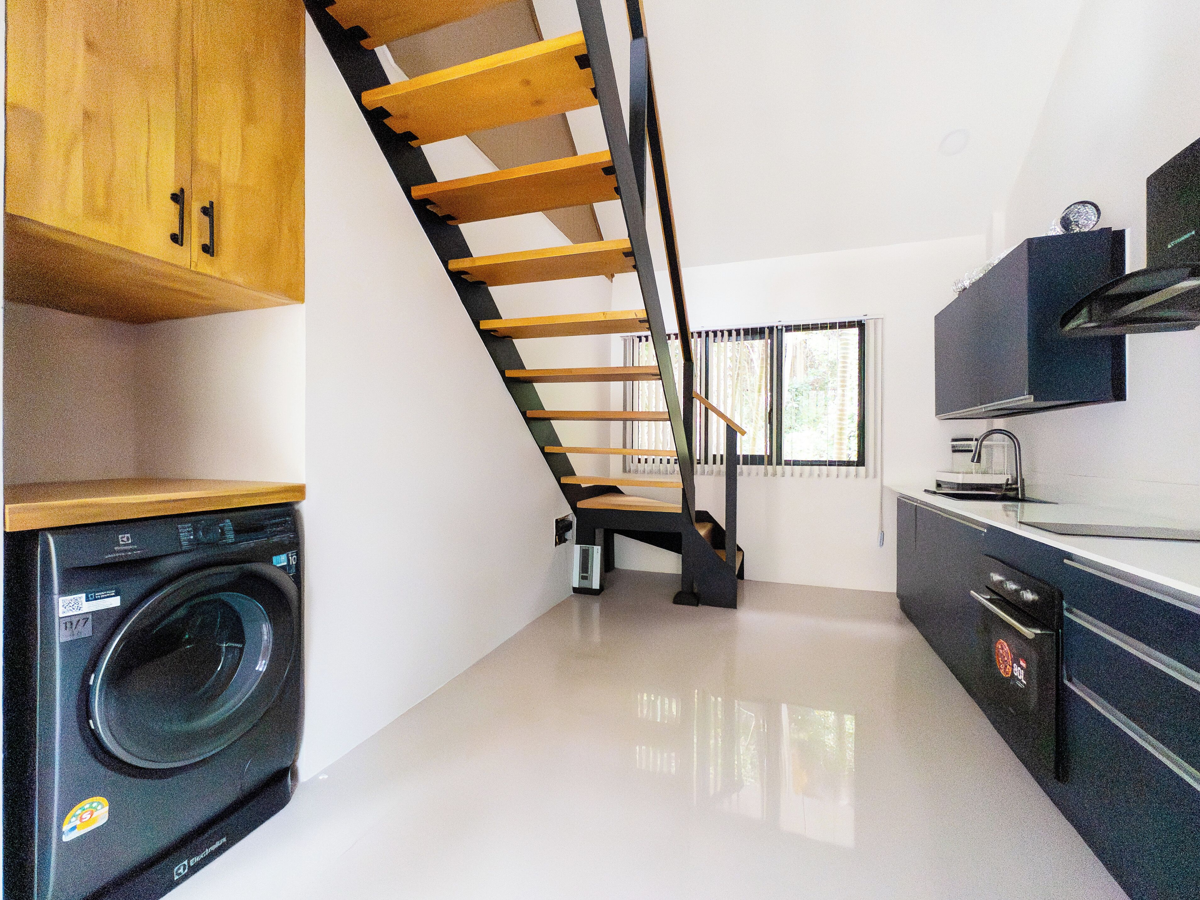 Cocina compacta con lavadora integrada, una escalera de madera y un diseño moderno.