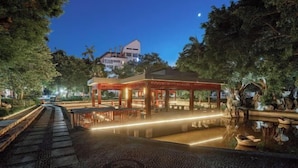 A traditional-style pavilion with a tiled floor and a small pond, surrounded by trees and a pathway leading to it. - Wuling Hotel (Liuzhou High-speed Railway Station) (Liuzhou)