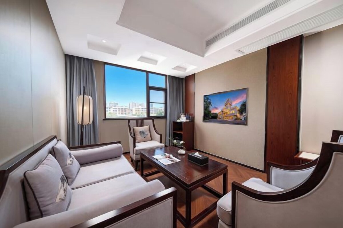 A hotel room with a sofa, armchair, coffee table, and a painting on the wall.