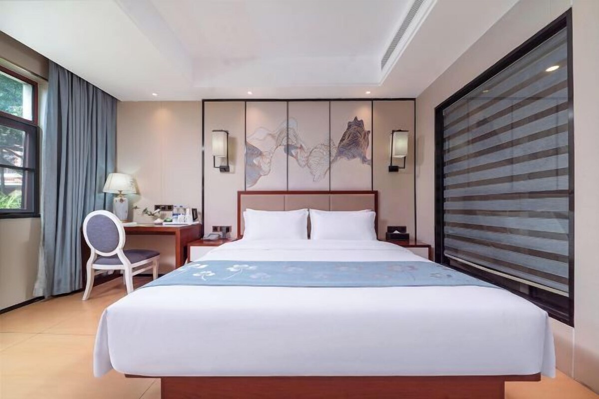 A hotel room with a large bed, a desk, a chair, and a window with curtains.