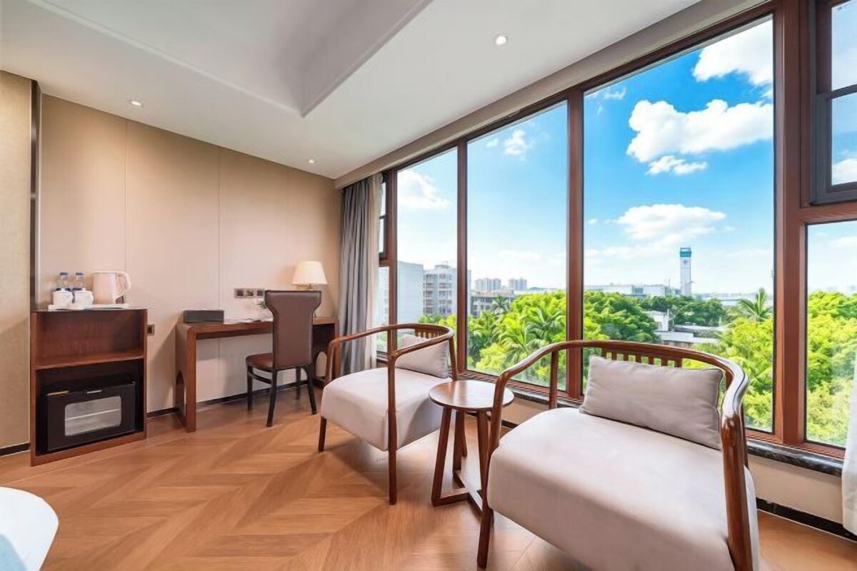A hotel room with a large window, a desk, a chair, and a sofa.