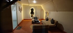 A cozy living room with a sofa, armchair, and a small table. A bear sculpture is mounted on the wall, and there's a door leading to another room.