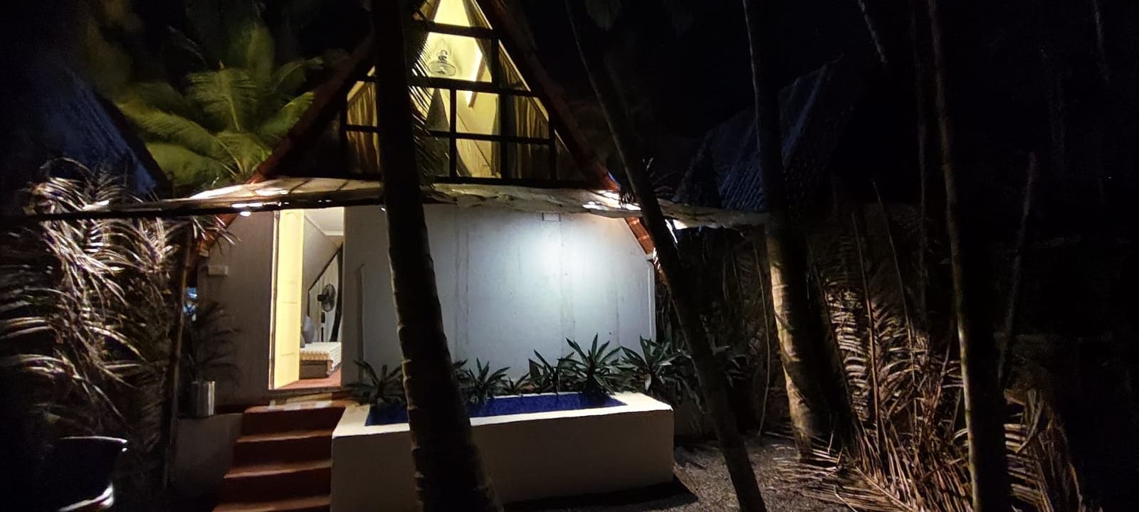 Una casa con techo de paja, una escalera que lleva a la entrada y una pequeña zona de piscina.