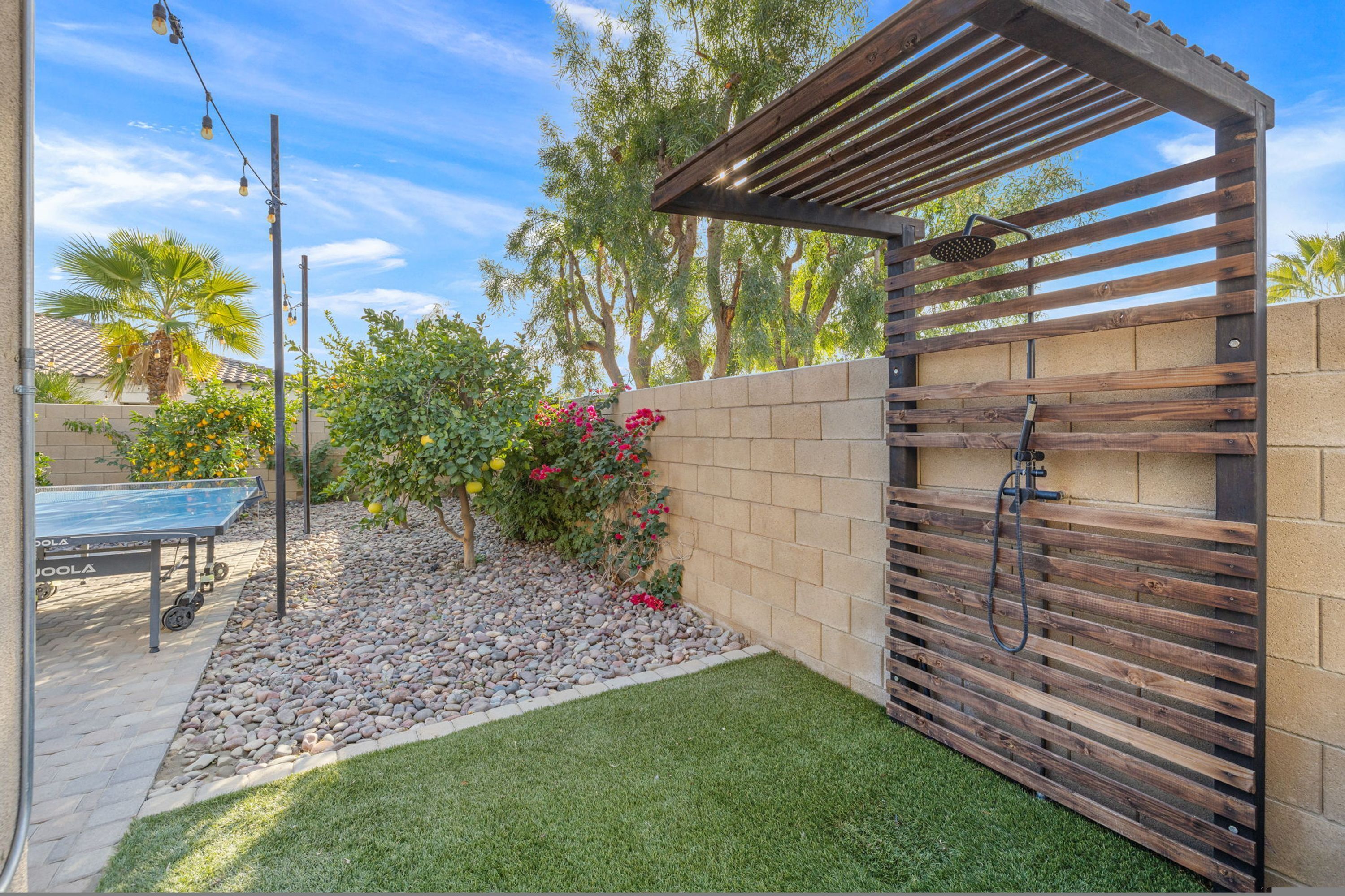 Un espace patio agrémenté d’une pergola, un petit jardin avec des galets et des plantes, et une table recouverte d’une nappe bleue.