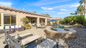 A modern house with a patio area featuring a pool, outdoor furniture, and a stone wall. - Relaxing Vacay Pool Spa Fire Pit Family Games (Indio)