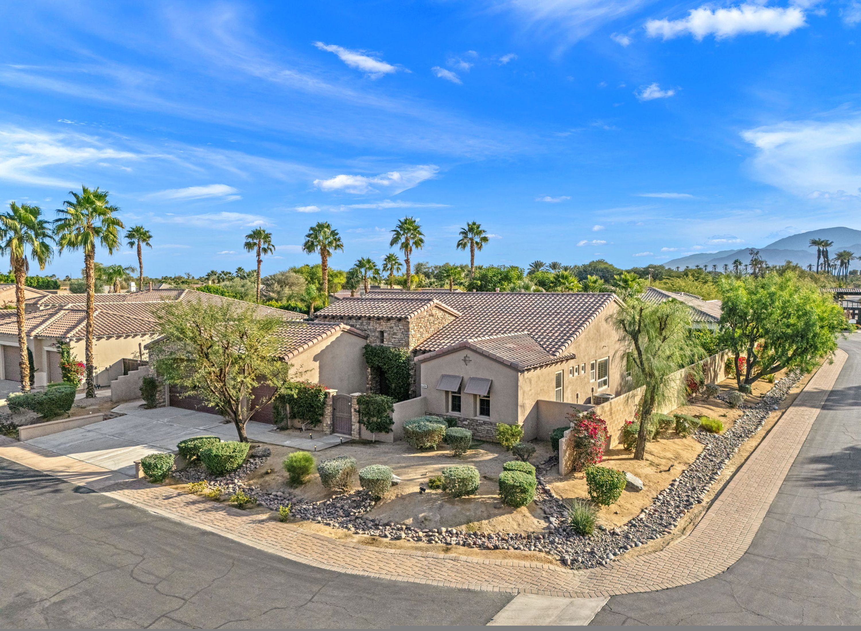 A residential area with houses featuring tiled roofs and surrounded by palm trees and landscaped gardens.