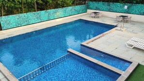 Una piscina rectangular con un área de terraza empavedada, una escalera pequeña y algunas sillas de descanso.