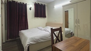 A small, well-lit bedroom with a single bed, a wooden table, and a wardrobe. - Annapurna Apartment-Khanal’s home (Kathmandu)