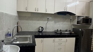 A kitchen with white cabinets, a black countertop, a sink, a kettle, a microwave, and a refrigerator. - Annapurna Apartment-Khanal’s home (Kathmandu)