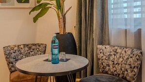 Een kamer met een ronde tafel, twee gestreepte stoelen, een potplant, een waterfles en een lijst met kunstwerk aan de muur.
