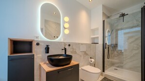 Een moderne badkamer met een grote, ovale spiegel, een zwarte wastafel, een toilet en een douche met glazen wanden.