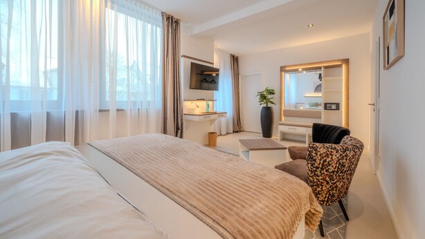 Een hotelkamer met een groot bed, een bureau met stoel, een spiegel en een plant.