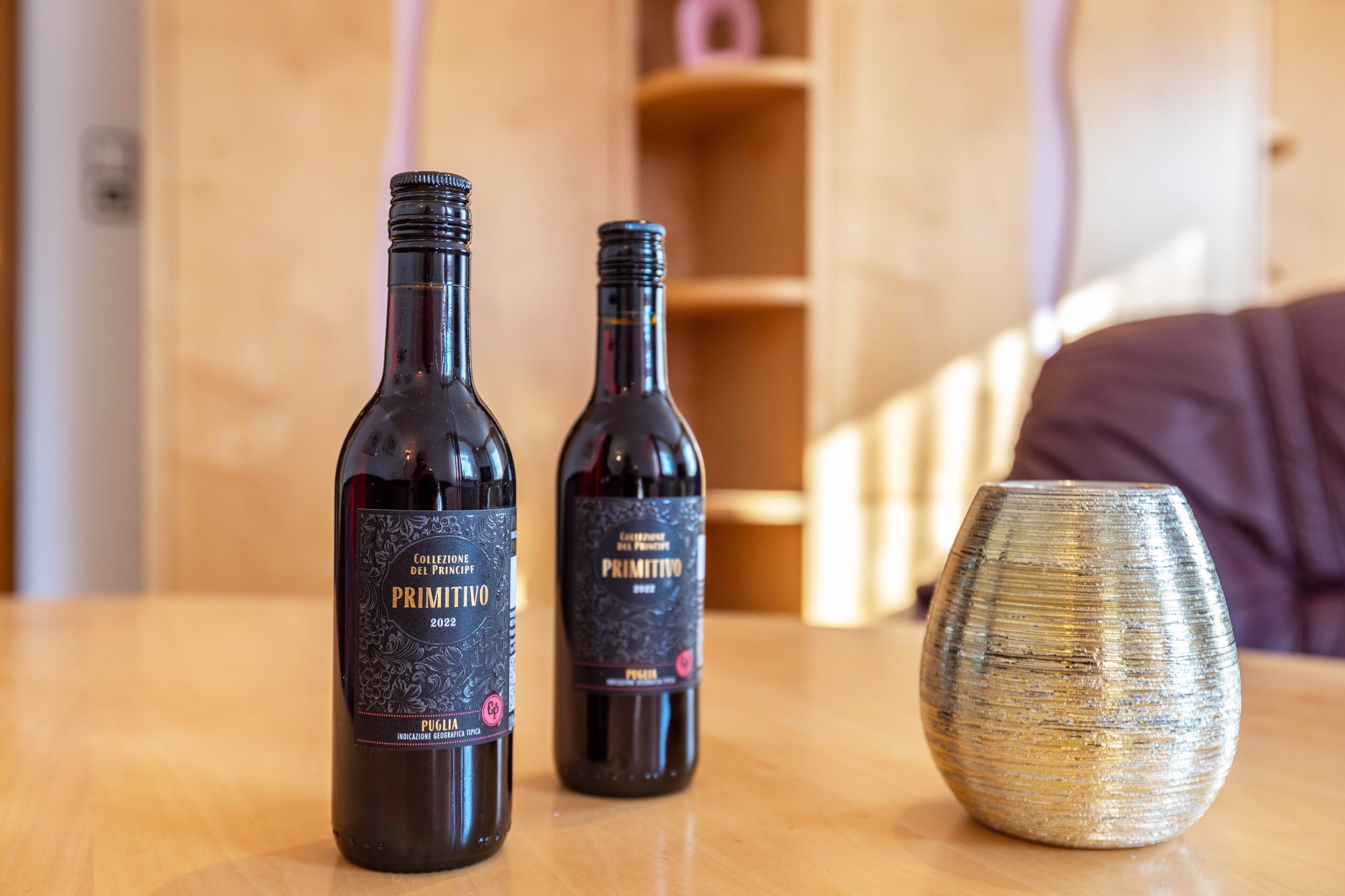 Two wine bottles and a ceramic vase on a wooden table.