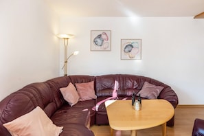 Una sala de estar con un sofá de cuero marrón, una mesa de centro de madera y dos cuadros abstractos enmarcados en la pared.