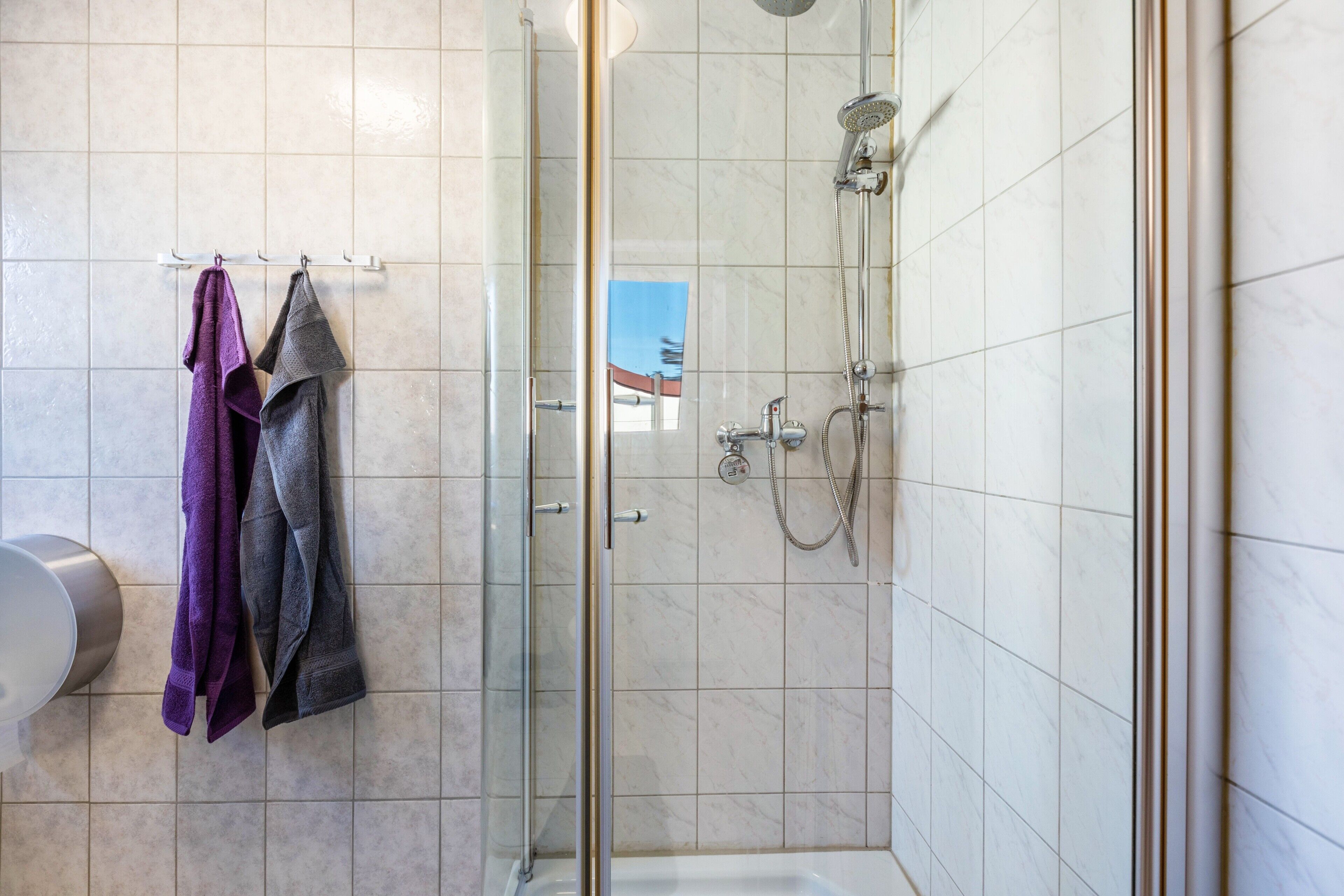 A shower with a glass door, a hand dryer, and a towel rack with two towels.