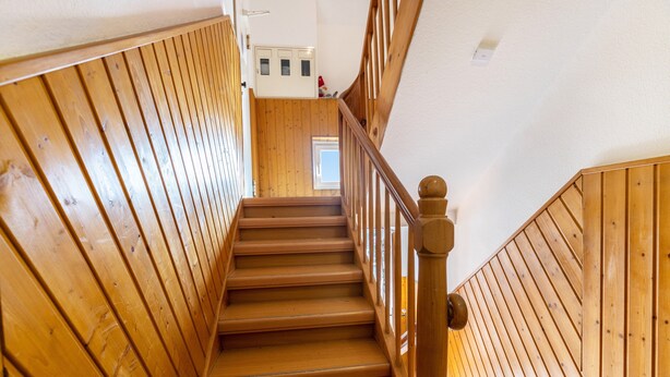 Una escalera de madera con barandilla, que sube a un piso superior.