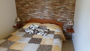 Una cama bien tendida, con un edredón a cuadros, un cabecero de madera y dos lámparas de noche con bases decorativas.