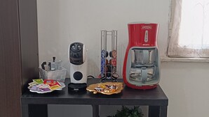 Una encimera de cocina con una cafetera, un hervidor, un plato de aperitivos y dos plantas en macetas.