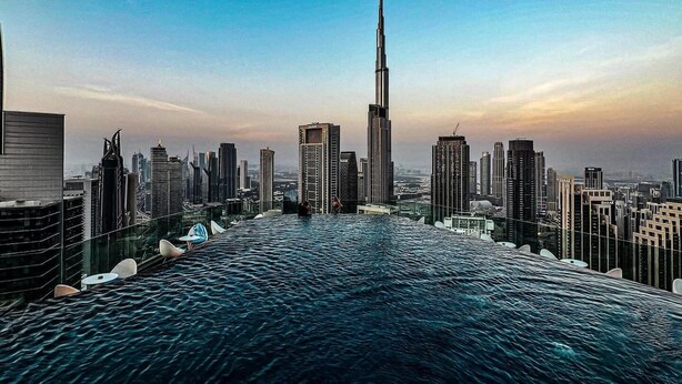 A cityscape with a prominent skyscraper, likely a hotel, with a view of the water and surrounding buildings. - Elegant 1BR Apartment, Rooftop 360° Infinity Pool with Burj Views (Dubai)