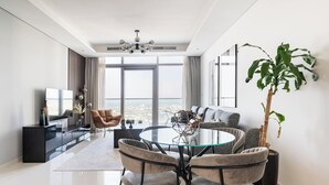 A modern living room with a glass dining table, comfortable seating, a large potted plant, and a city view through large windows. - Elegant 1BR Apartment, Rooftop 360° Infinity Pool with Burj Views (Dubai)