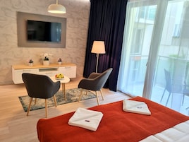 Hotellihuone, jossa on sänky, kaksi tuolia, työpöytä, jossa on televisio, lamppu ja näkymä ulos.
