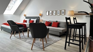 A modern loft bedroom with a skylight, a sofa, chairs, a dining table, and a wall-mounted lamp. - B40 Green ApartRooms (Budapest)