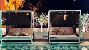 Due poltrone da esterno con tende parasole, una piscina con piastrelle e alcune palme sullo sfondo.