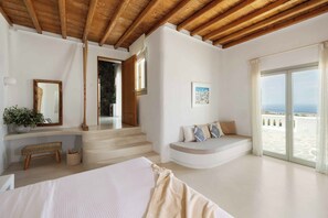 A modern bedroom with a large bed, a bench, a staircase, and a balcony with a view. - MyKer Estate | 8-BDR, Luxury, Seaview, Pool Villa (Mykonos)