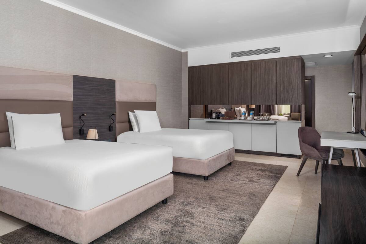 Una camera d'albergo moderna con due letti, un angolo cottura e una scrivania.