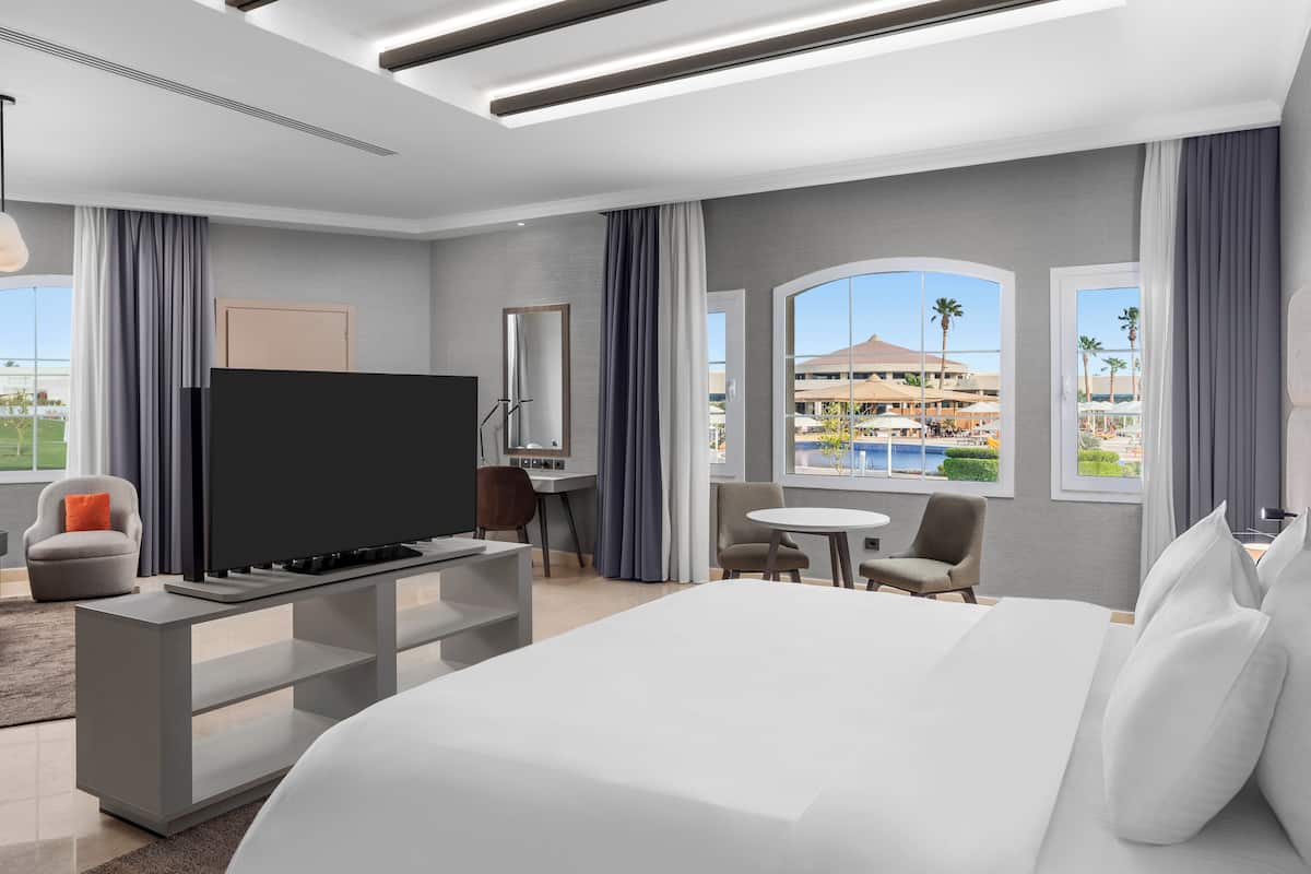 Camera d'albergo moderna con un grande letto, una TV a schermo piatto, una scrivania e vista sul resort.