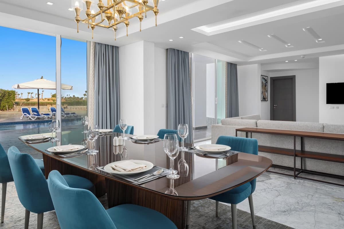 Un'area pranzo moderna con tavolo in vetro, sedie blu e vista sulla piscina.