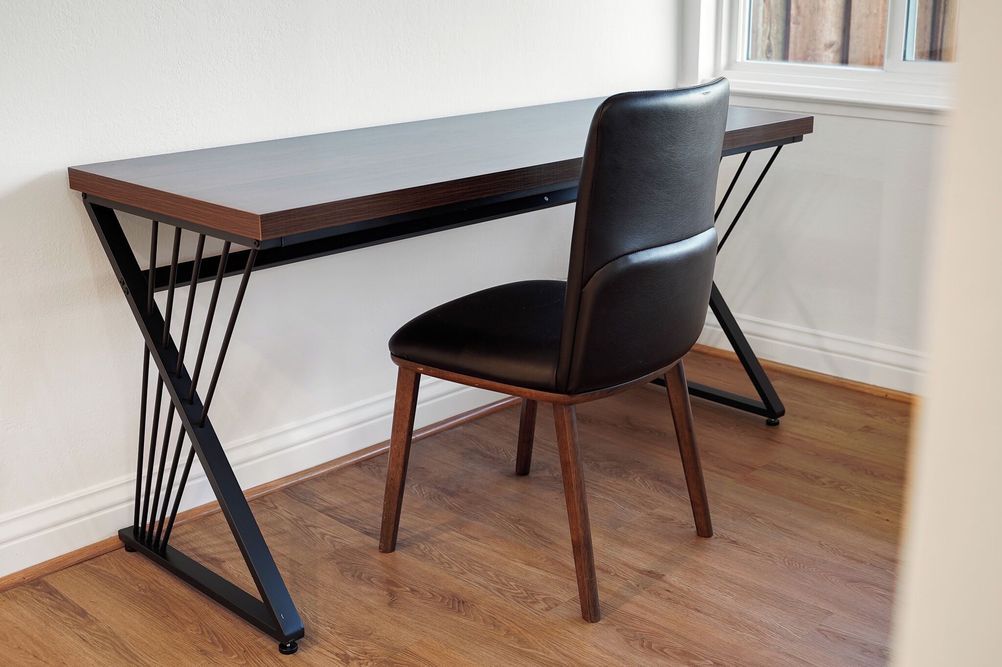 A modern desk with a sleek design, positioned next to a chair with a high backrest.