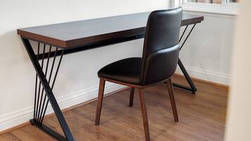 A modern desk with a sleek design, positioned next to a chair with a high backrest.