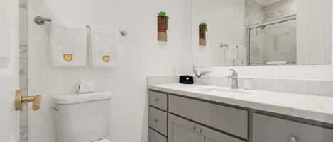 Un baño moderno con inodoro, lavabo y tocador. Hay toallas colgadas en un perchero y un espejo sobre el lavabo.