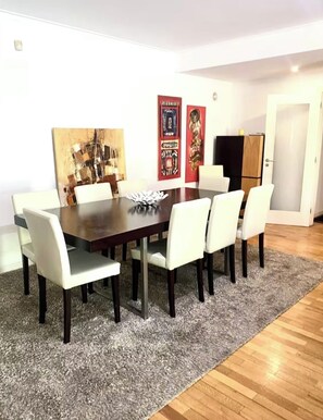 A dining area with a rectangular table, six chairs, a grey rug, and artwork on the walls.